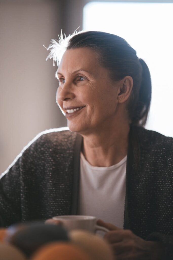 A cheerful senior woman smiles while enjoying a cup of coffee indoors.