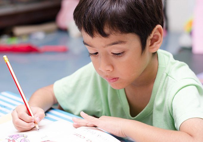 A young boy in a green shirt intently writes in a notebook, demonstrating focus and engagement in his learning process.