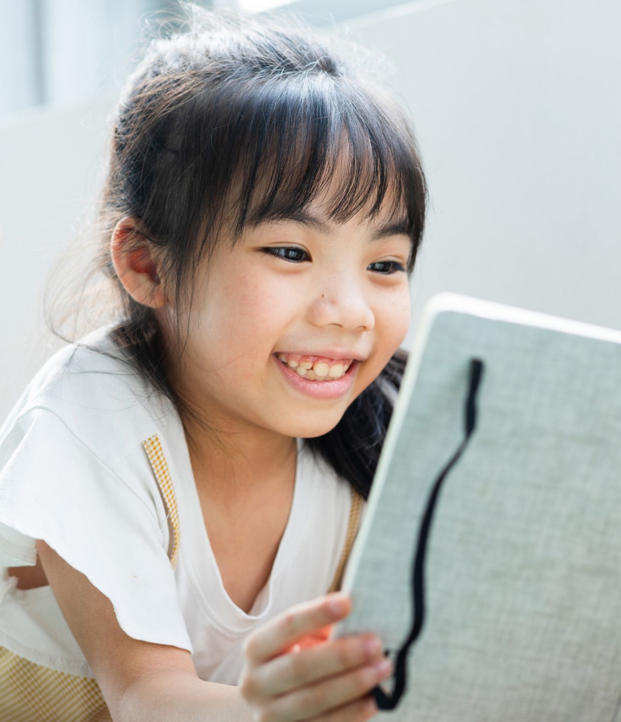 A joyful young girl smiles as she interacts with a tablet, showcasing engagement and curiosity in a bright, modern setting.